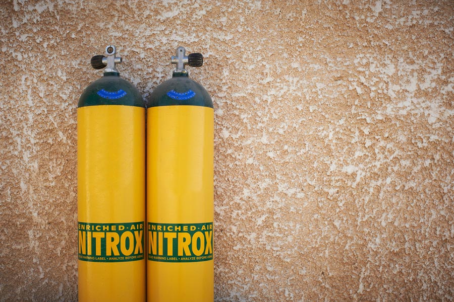 two yellow and green nitrox tanks against textured beige wall