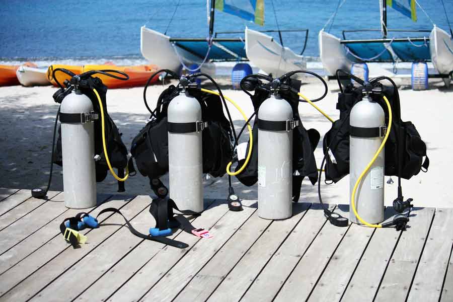 scuba tanks and BCDs lined up on the beach
