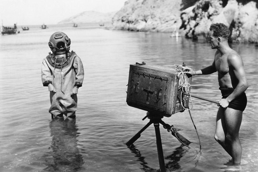 man in vintage scuba diving gear posing for a photo on the beach