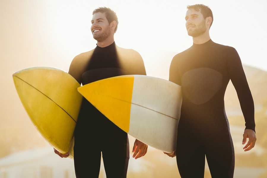 two male surfers in wetsuits carrying surfboards