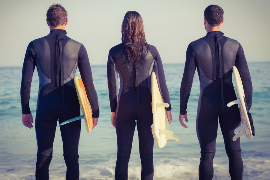 three surfers in wetsuits facing the beach